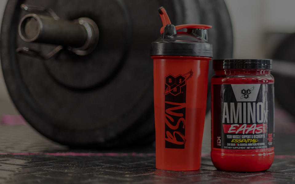 tub of aminox eaas beside a shaker in front of a barbell